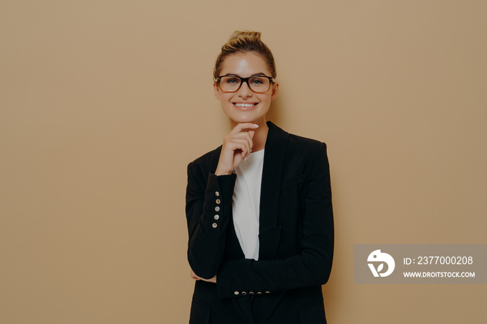 Confident european young female in spectacles and black blazer over white tshirt touching her chin tenderly