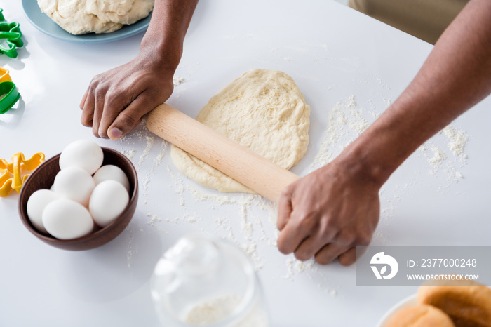 Cropped close-up view of his he guy hands making fresh handmade bread pizza pie cake rolling dough bakehouse craft on table desktop using pin in modern light white interior house kitchen