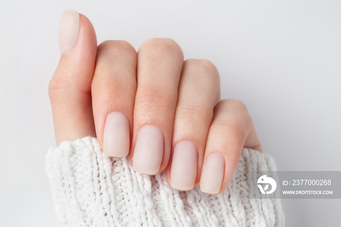 Matt nude nails close up on the light background. Winter manicure, woman hand in the warm sweater