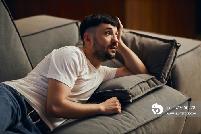 A young man in a white T-shirt, exhausted, fell asleep in front of the TV. Lazy man watching television at night alone.