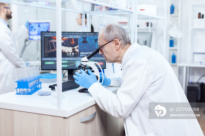 Senior scientist preparing and analyzing microscope slides with busy coworkers. Chemist researcher in sterile lab doing experiments for medical industry using modern technology.