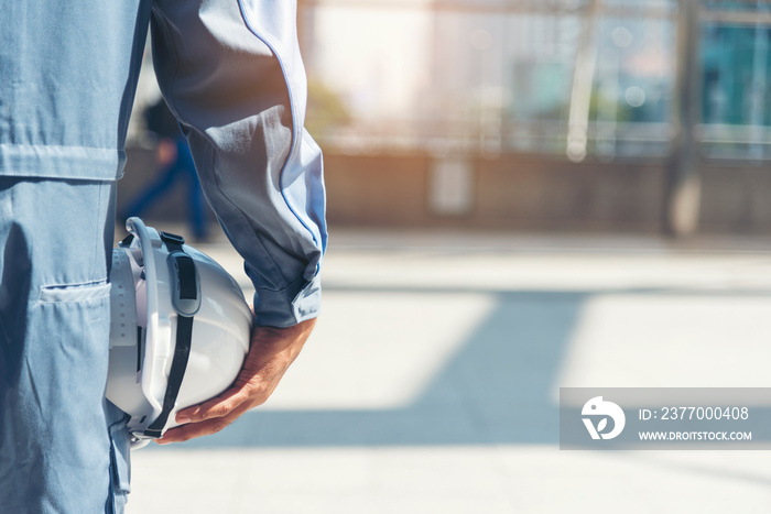 Engineer man hands holding hardhat white work helmet hard hat for Construction Engineering. Construction engineer man in safety suit hands hold white worker helmet hard hat on site City Engineering