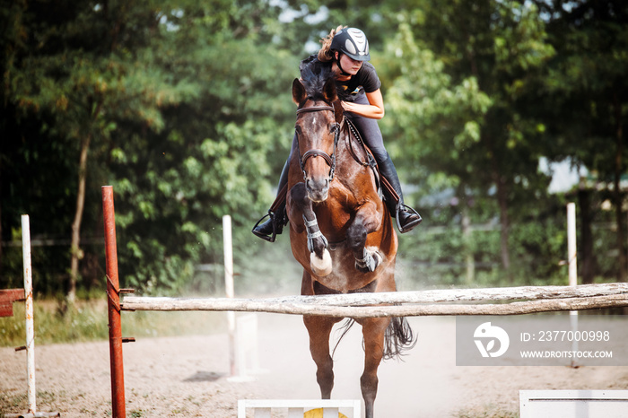 Young female jockey on horse leaping over hurdle