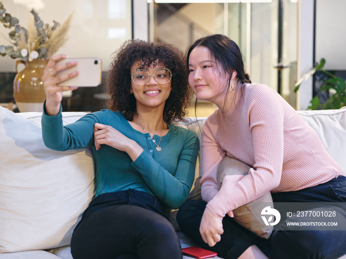 UK, London, Two female coworkers taking selfie in modern office lobby