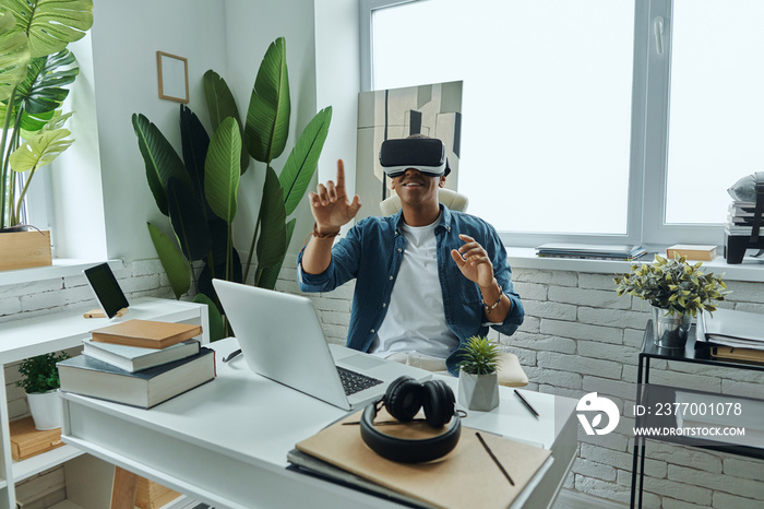 Happy African man wearing virtual reality glasses while sitting at working place