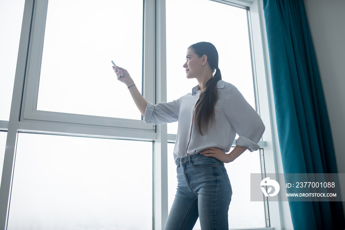 Concentrated lady using a remote control for closing the blinds