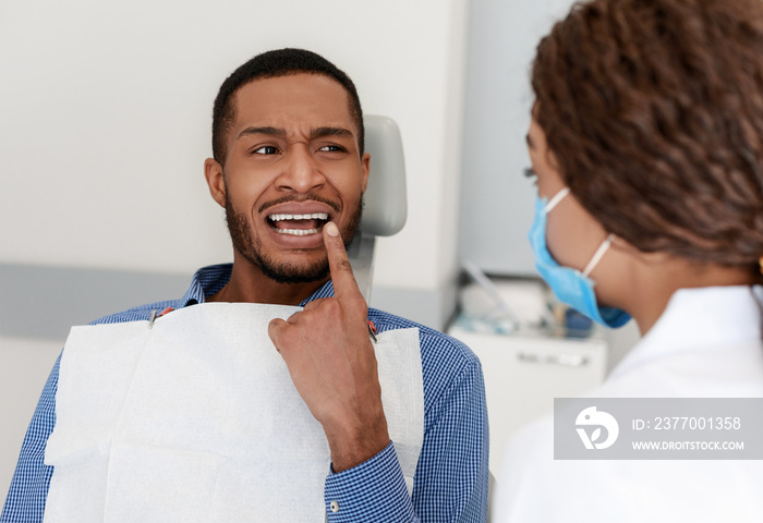 Black guy visiting dentist, showing doctor painful teeth