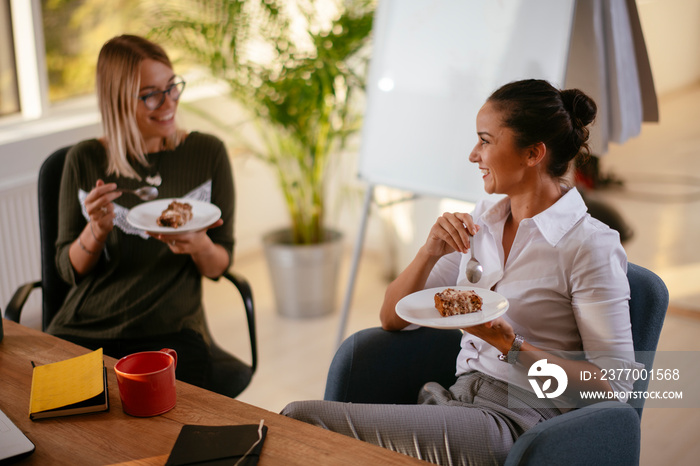 Two smiling women in the office eating cake