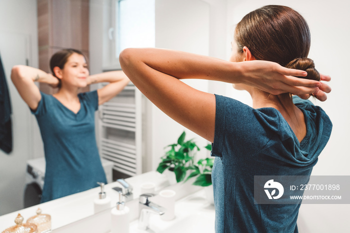 Back view of young woman standing in front of the mirror in the bathroom getting ready for sleep waring her night gown