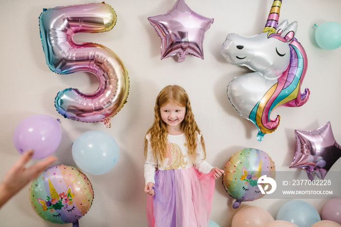 Happy and surprised girl celebrates her birthday. Party decoration with balloons in the style unicorn, rainbow, my little pony. Birthday party for 5 years. Idea for decorating party.