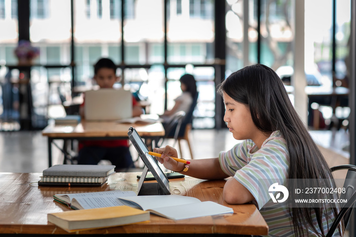 Side view of a girl holding a pen pointing at the tablet screen The book is placed on the table the sides are blurred.