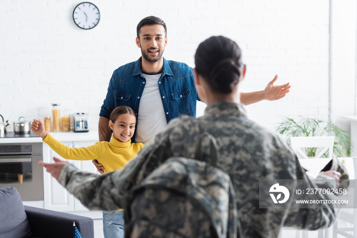 Smiling family looking at blurred mother in military uniform at home