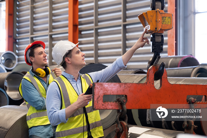 Selective focus at Caucasian men mechanical engineer, wearing safety equipment. While doing machine maintenance and safety control inside of factory area. With blurred background of heavy machine.