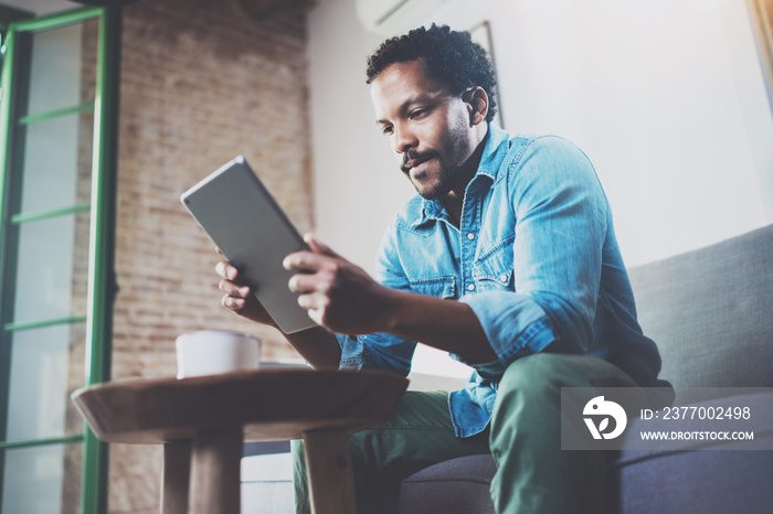 Pensive African man using tablet for video conversation while relaxing on sofa in modern office.Concept of young business people working at home.Blurred background.Selective focus.