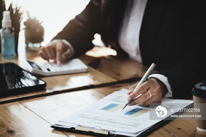 A businesswoman examines financial documents and uses a calculator to research the income affected by the coronavirus pandemic to adjust her marketing strategy.