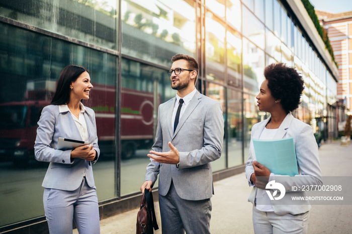 Three young business people talking to each other while walking outdoors.