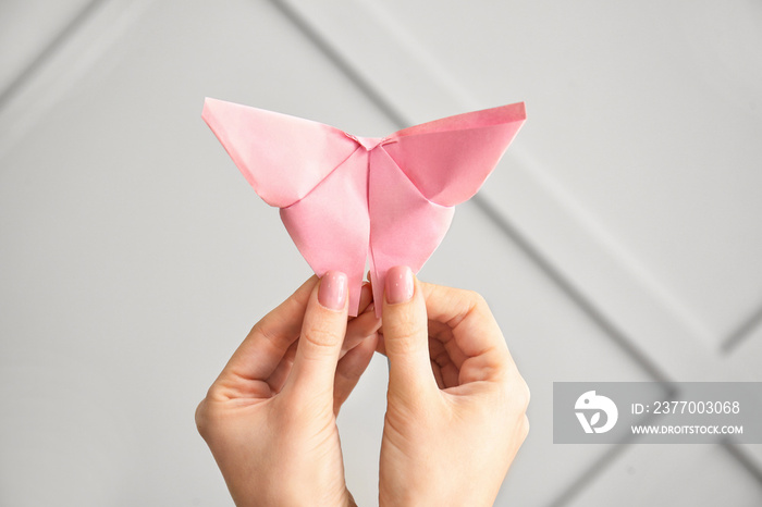 Female hands with origami butterfly on light background