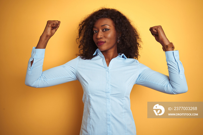 African american businesswoman wearing elegant shirt over isolated yellow background showing arms muscles smiling proud. Fitness concept.