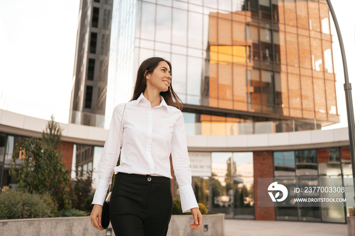 Smiling Caucasian woman in business wear walking near the urban business center