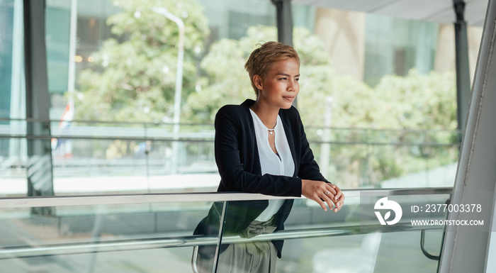 Successful businesswoman leaning on glass railing on a modern office balcony