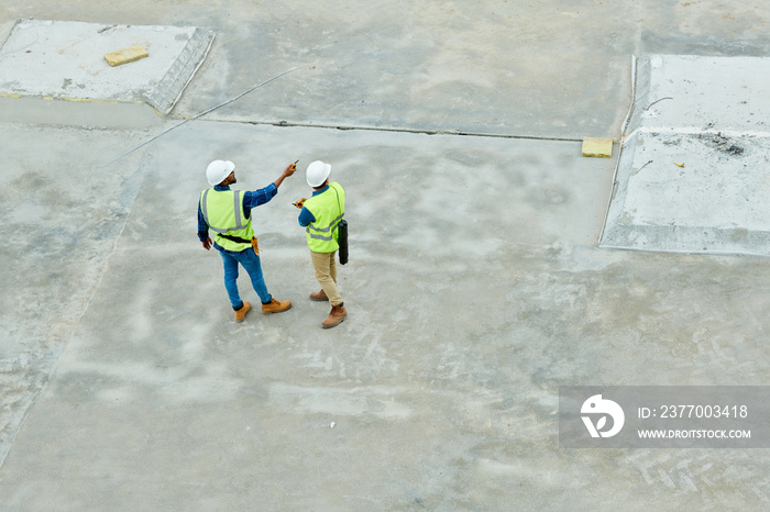 Top view portrait of two workers standing on concrete floor of construction site and planning project, copy space background