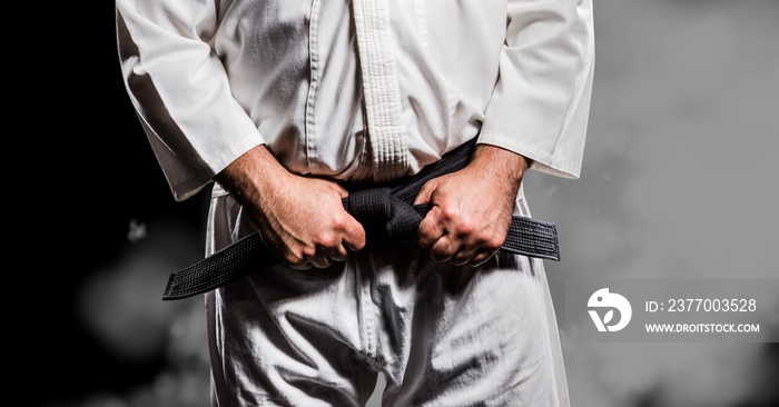 Composition of midsection of caucasian male martial artist with black belt over smoke on black