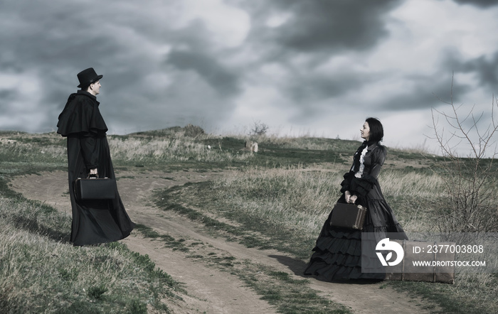 Outdoors portrait of a victorian lady in black and gentleman standing on the oppisite sides of the road.