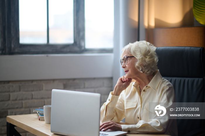 Woman looking at window sitting at table with laptop