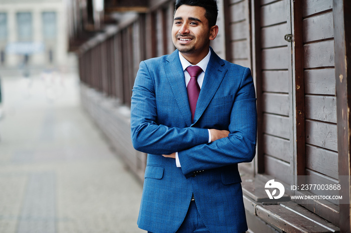 Elegant indian fashionable man model on suit posed against wooden stalls.