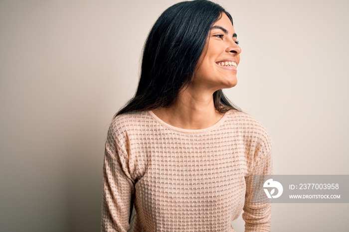 Young beautiful hispanic woman wearing elegant pink sweater over isolated background looking away to side with smile on face, natural expression. Laughing confident.