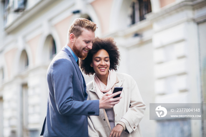 Two business people in an informal conversation in front of a business building, man using phone.