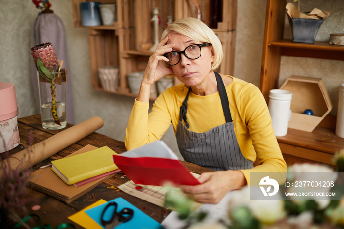 Portrait of female business owner holding red envelope while doing accounting in flower shop, copy space