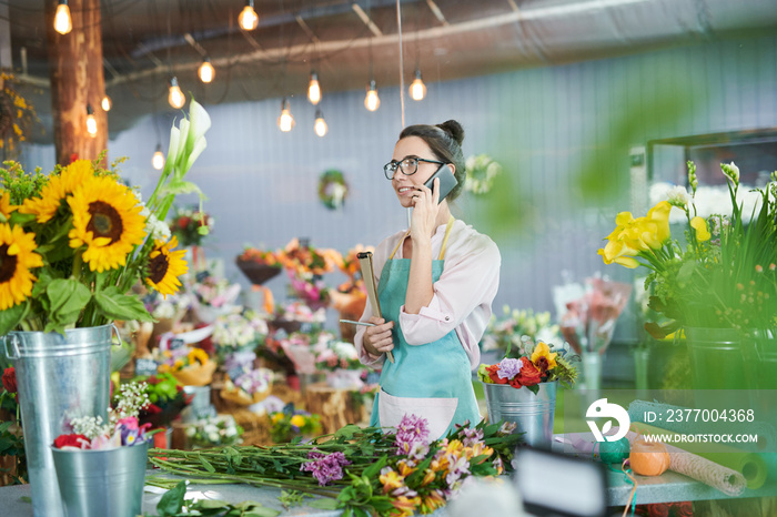 Side view portrait of young woman speaking by phone in flower shop