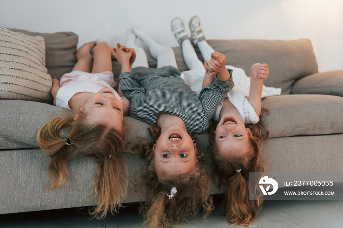 Girls laying down on the sofa upside down and smiling. Group of children is together at home at daytime