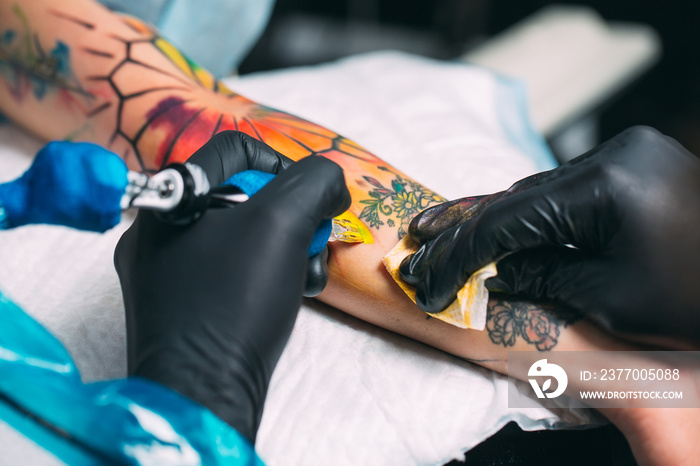 Professional tattoo artist makes a tattoo on a young girl’s hand.