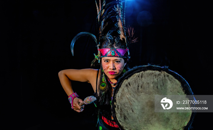 close up of young woman Teotihuacana, Xicalanca - Toltec in black background, with traditional dress dance with a trappings with feathers and drum