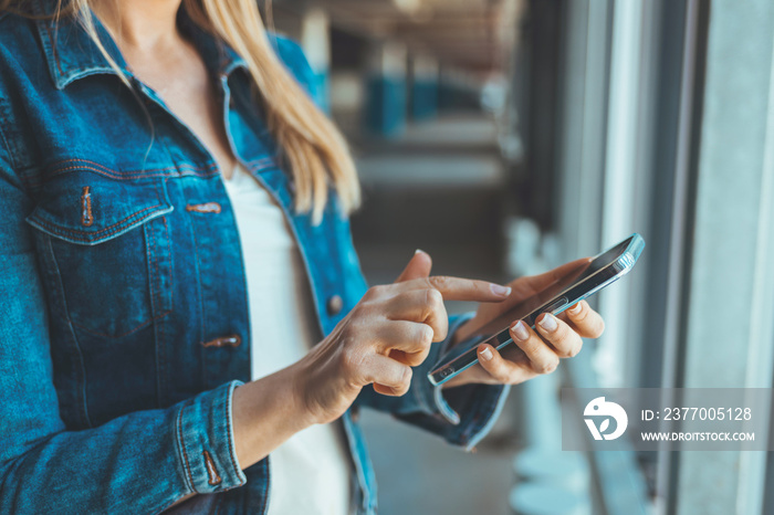 Photo of Young business woman wearing casual clothing calling mobile phone while standing with blurred car in parking lot. Side view of Beautiful, happy Caucasian female using smartphone device