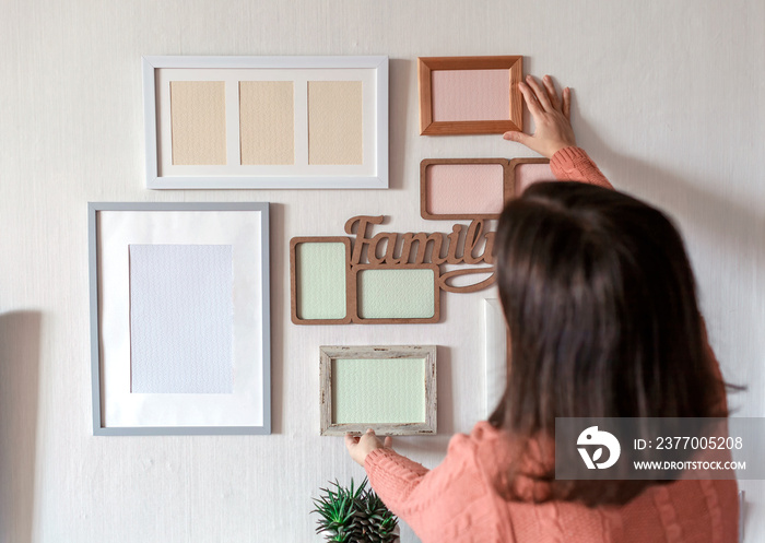 Girl hanging frame on white wall with set of different empty vertical and horizontal picture frames to create family photo gallery, to capture a moment, mockup template on white background, lifestyle