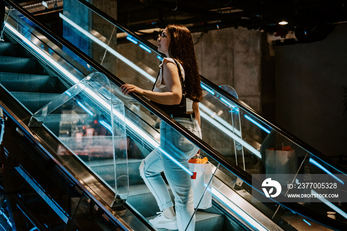 Young brunette Latina attractive woman with shopping bags on escalator in the fashion store mall.