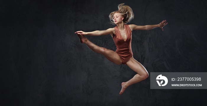 Young graceful ballerina dances and jumps in a studio. Isolated on a dark background.