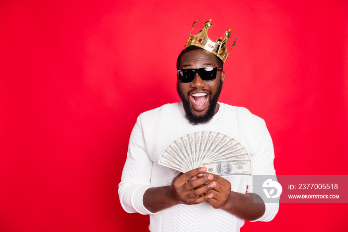 Portrait of amazed surprised crazy funky dark skin man with brown hair beard hold fan money win jackpot in x-mas casino got profit become millionaire wear white jumper isolated red color background