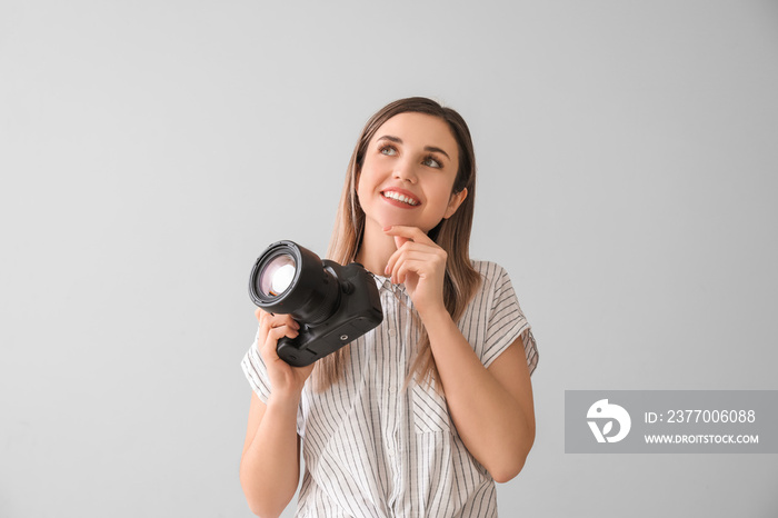 Thoughtful female photographer with modern camera on grey background