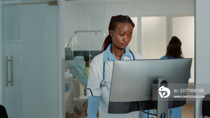 Woman working as doctor with stethoscope using computer to find patient documents for information in hospital ward. Medic with white coat looking at monitor to check healthcare system.