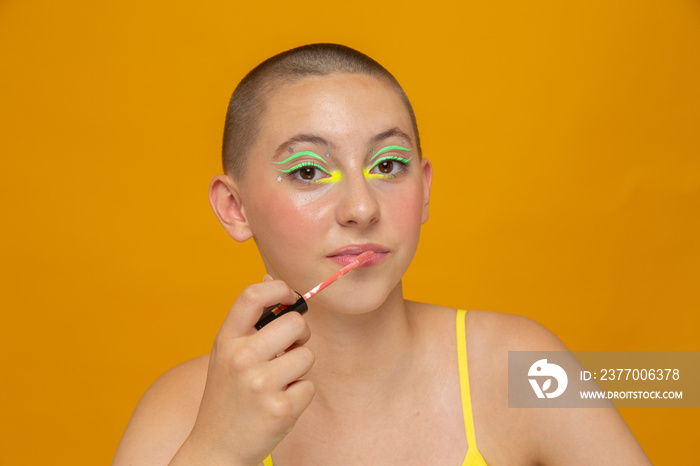 Studio portrait of girl with neon colored make-up applying lip gloss