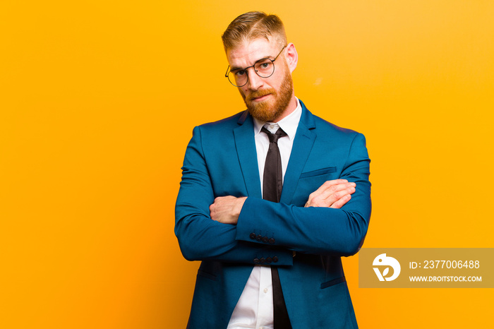 young red head businessman feeling displeased and disappointed, looking serious, annoyed and angry with crossed arms against orange background