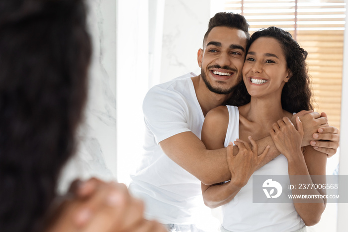 Affectionate Millennial Couple Looking At Mirror And Cuddling In Bathroom