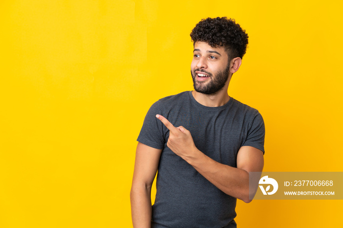 Young Moroccan man isolated on yellow background surprised and pointing side