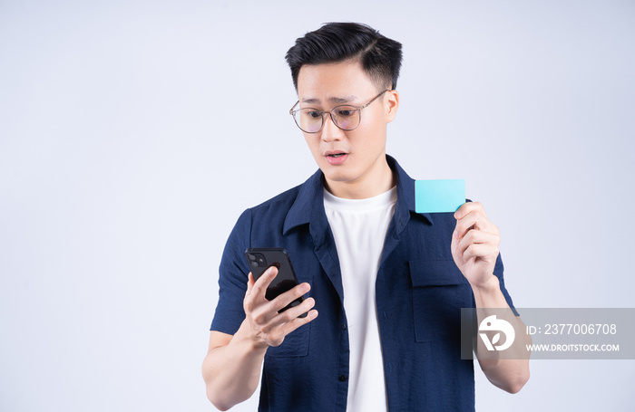 Image of young Asian man holding bank card on white background