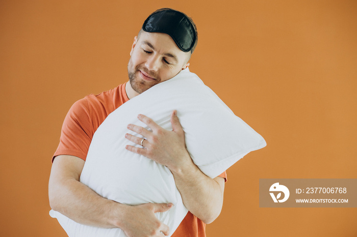 Young man hugging his pillow and wearing sleeping mask