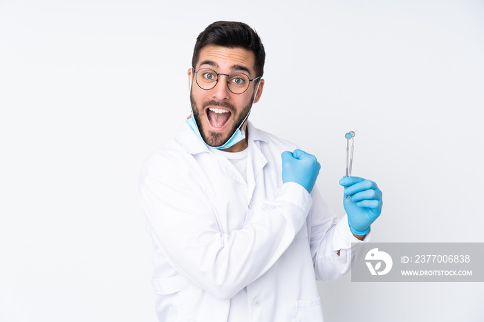 Dentist man holding tools isolated on white background celebrating a victory